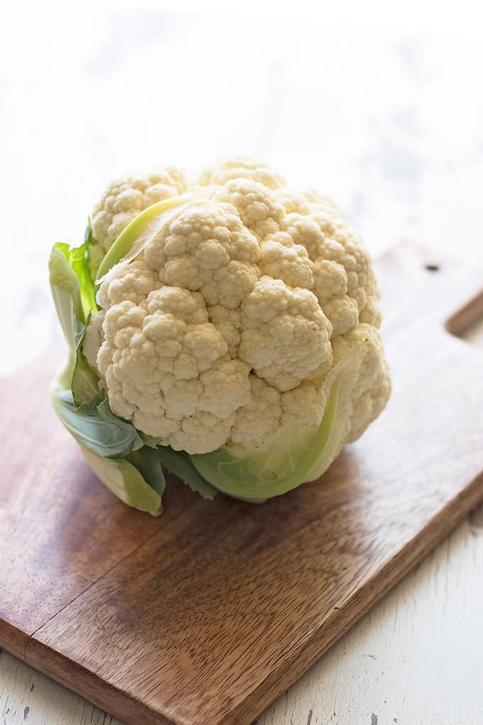 Whole head of cauliflower on a brown wooden cutting board.