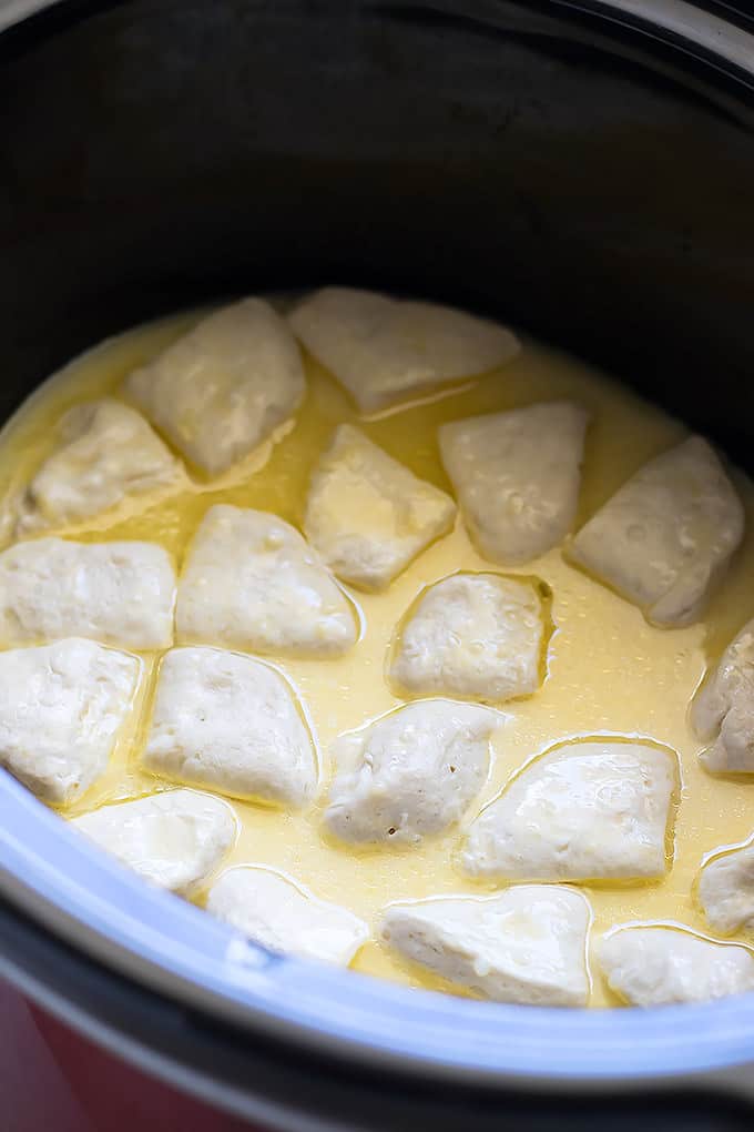white dumpling in a yellow broth in a black slow cooker.