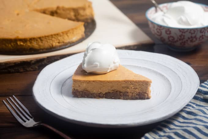 Ultimate Pumpkin Cheesecake with whipped cream on a white plate.