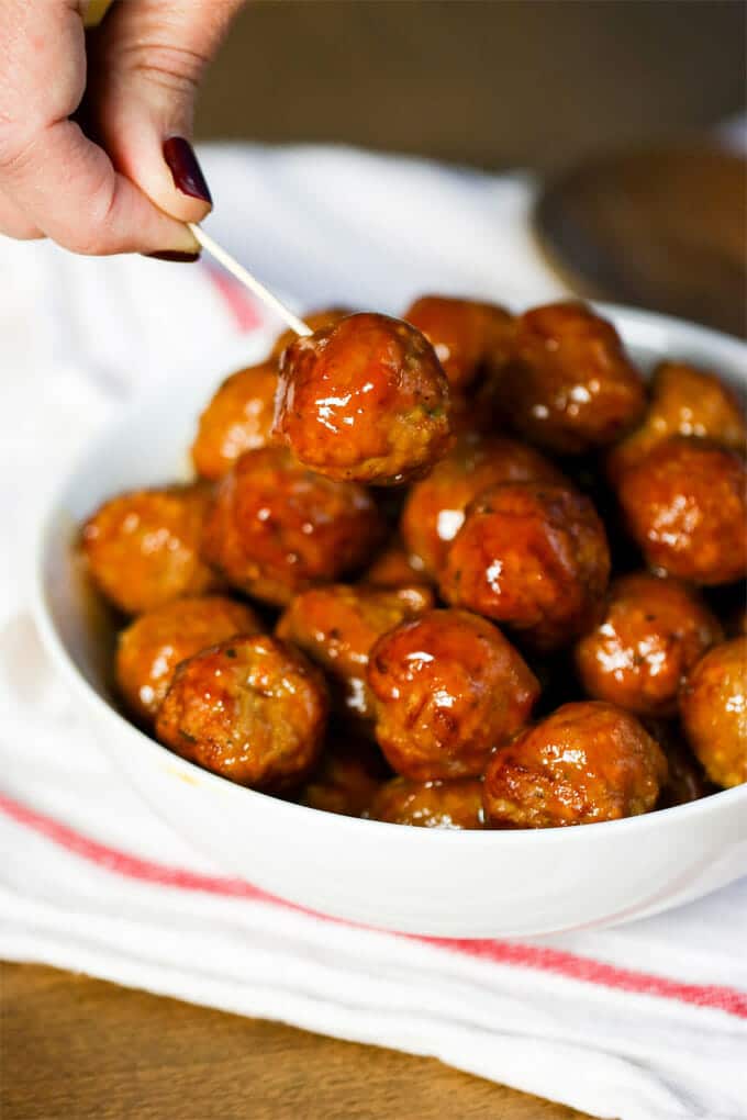 White bowl filled with cooked meatballs that have been tossed in a red sweet and sour sauce.
