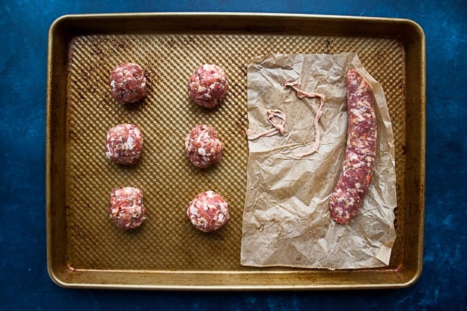 Raw sausage and meatballs on baking sheet.