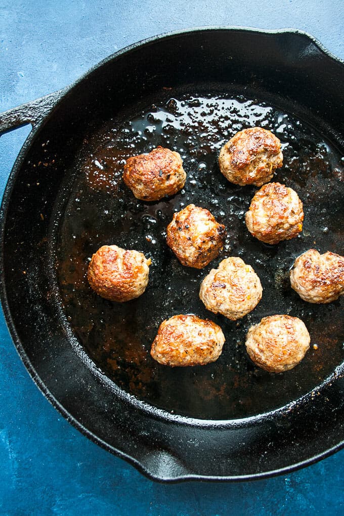 Black cast iron skillet with meatballs that have been browned.