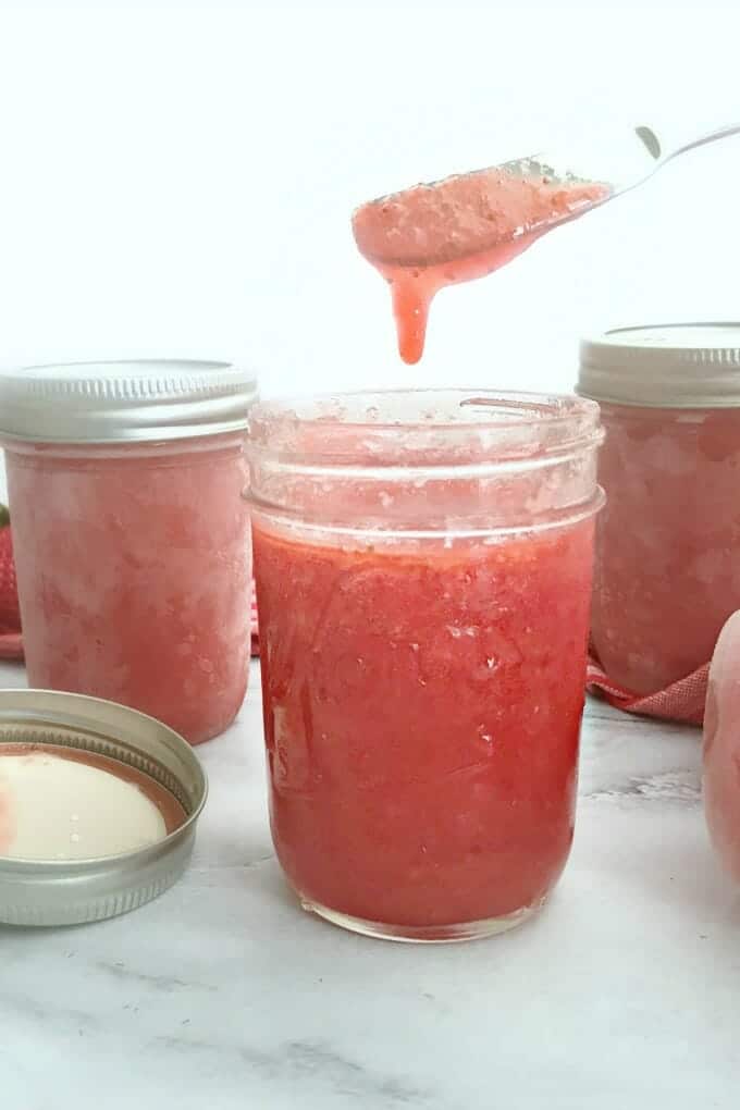 Cans of strawberry freezer jam with a knife of dripping jam.