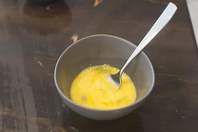 Raw eggs in gray bowl with a fork that has been used to whisk them.