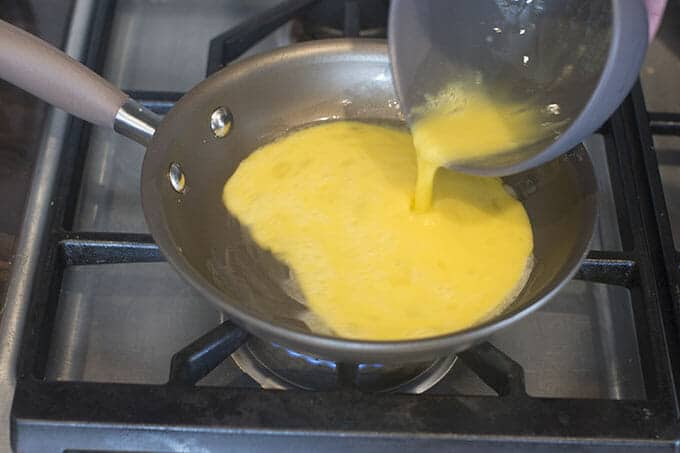 Whisked eggs being poured into a pan on the stove.