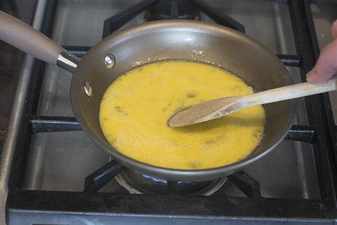 Raw eggs being stirred with a wooden spoon on the stove.