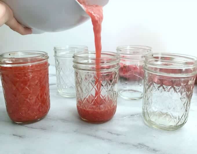 Freezer jam being poured into glass mason jars.