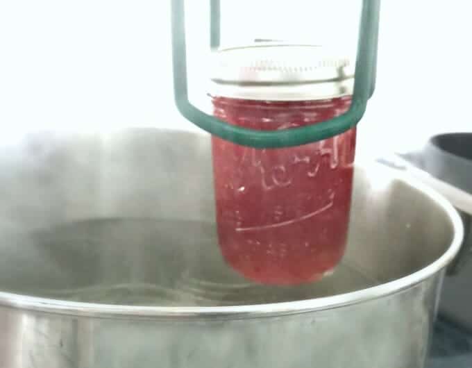 Filled glass jar with lid being put back into pot of hot water.