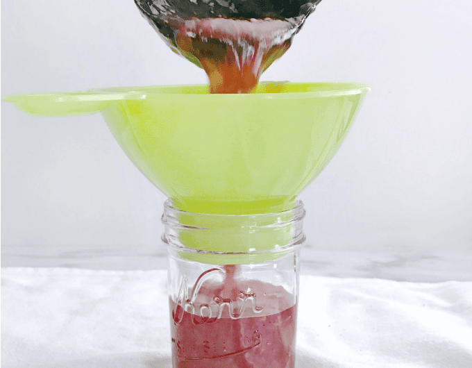 Jam being poured into a glass jar via a yellow funnel.