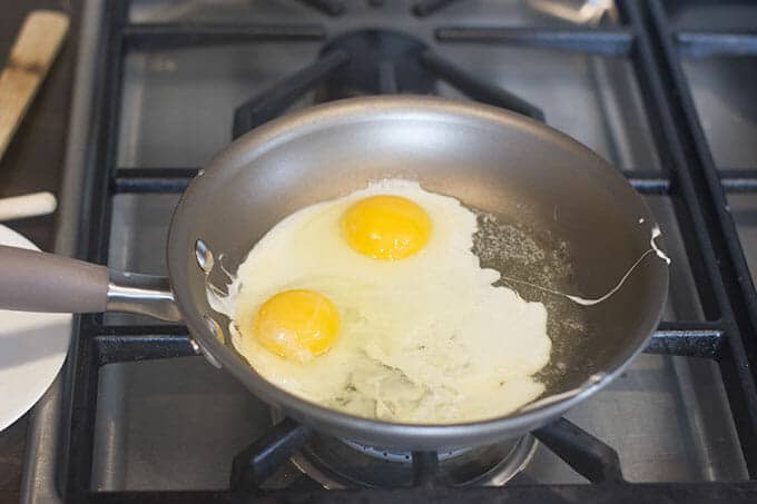 Two eggs in a pan, yolks surrounded by setting egg whites.