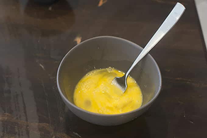 Raw eggs in bowl with the fork that has been used to whisk them.