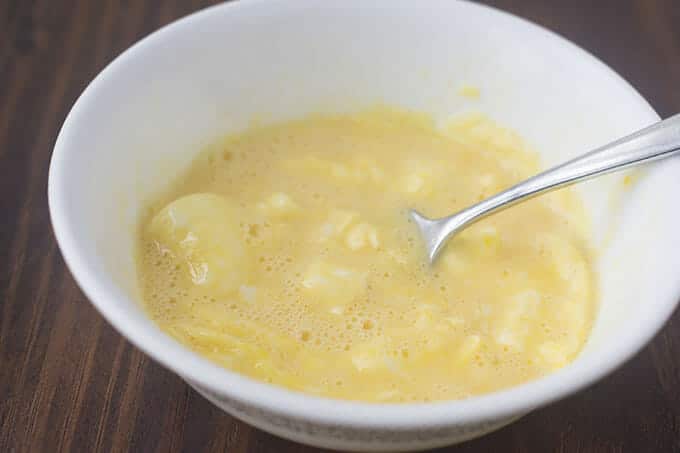 Partially cooked scrambled eggs being stirred in a white bowl.