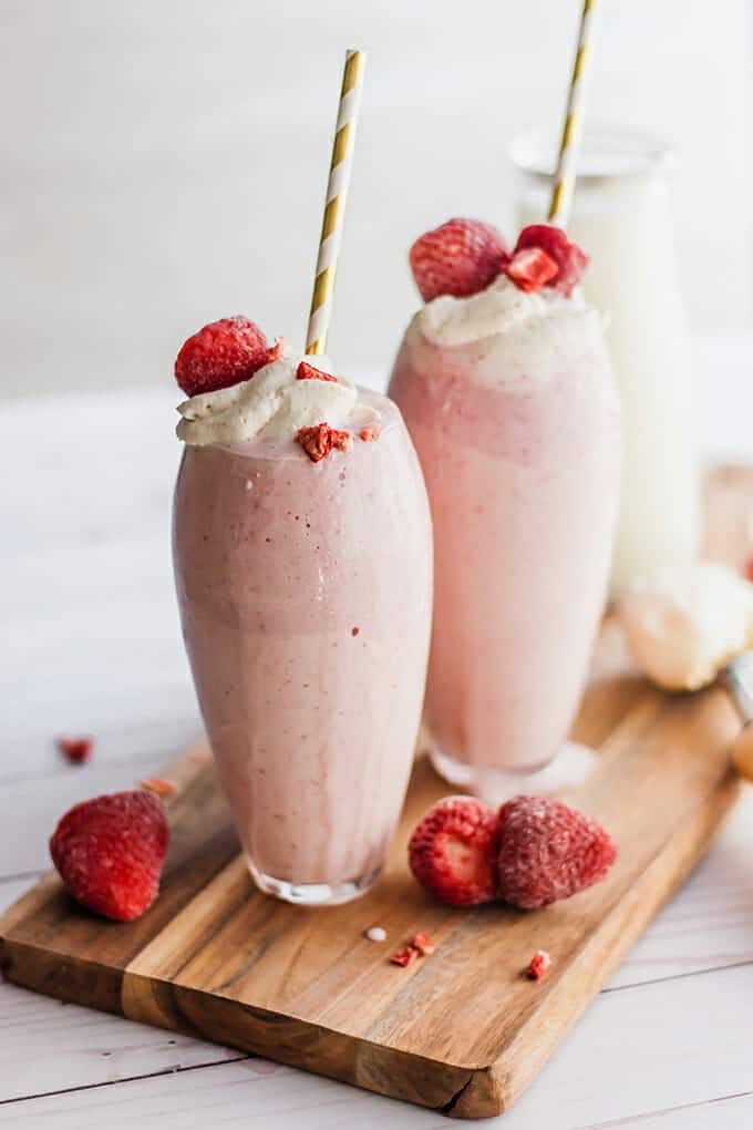 Strawberry milkshakes in glasses with straws, topped with whipped cream and berries.