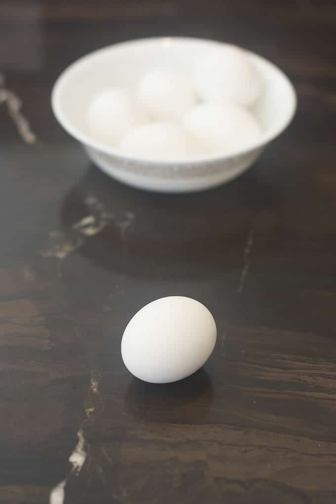Hard boiled egg on counter with bowl of eggs in background.