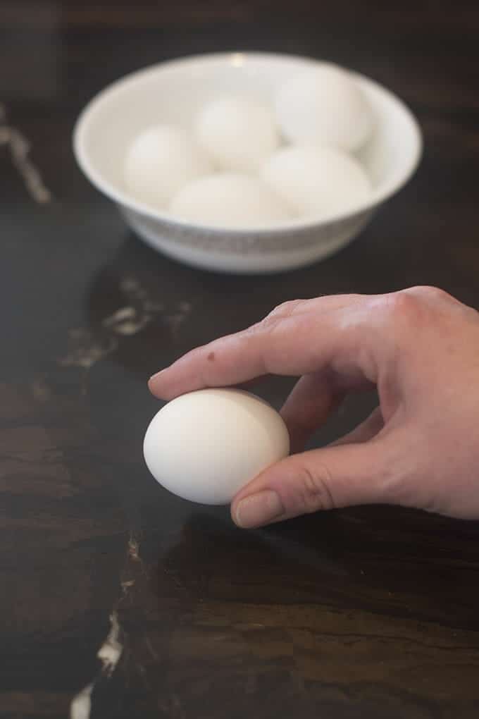 Holding a hard cooked egg between fingers to tap it on the counter.