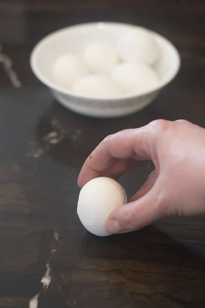 Holding a hard cooked egg, to tap the top and bottom on the counter.
