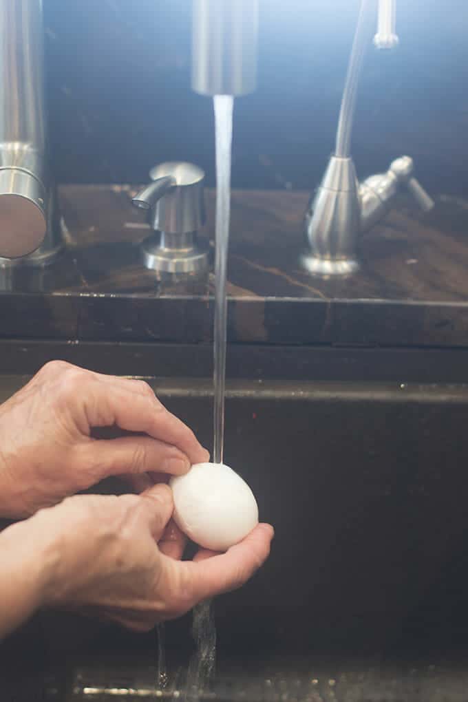 Egg being peeled under a stream of water from the tap.
