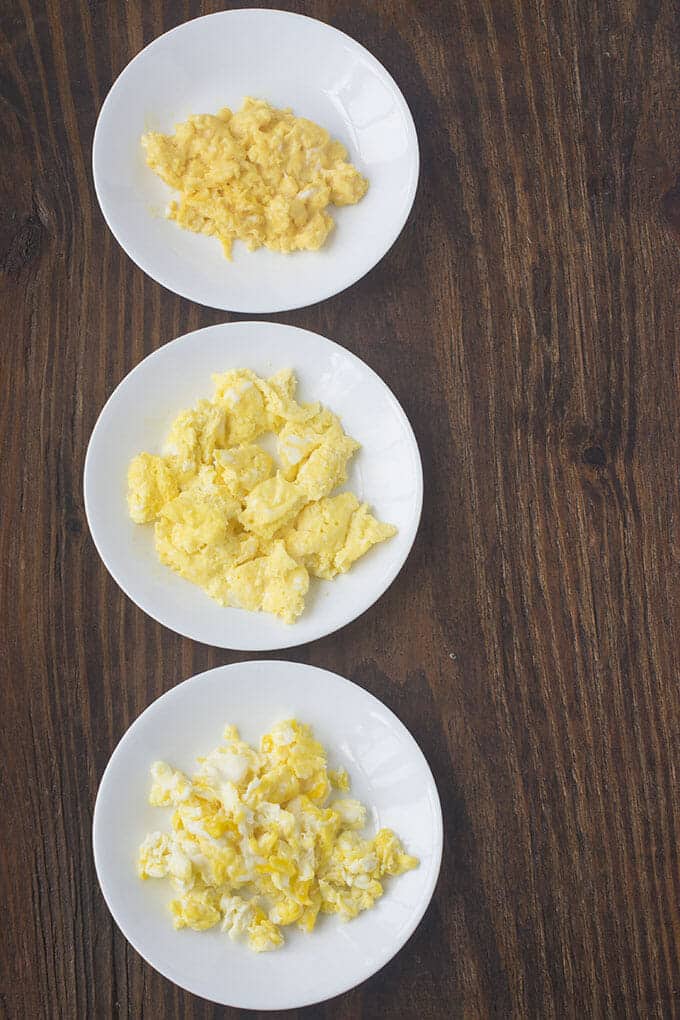 Three white plates each with scrambled eggs, slightly varied in appearance.