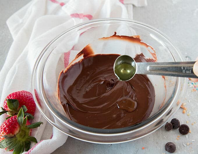 Adding a teaspoon of oil to melted chocolate in a glass bowl.