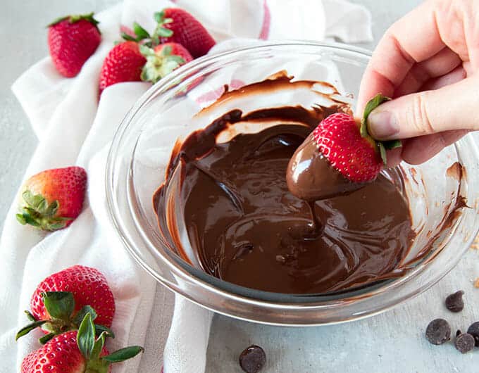 Strawberry being held by the stem to dip in melted chocolate.