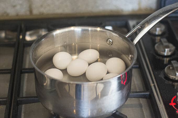 Saucepan with water and multiple eggs on the stovetop.