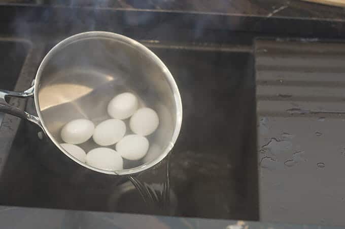 Steaming water being drained from a pan with eggs in it.