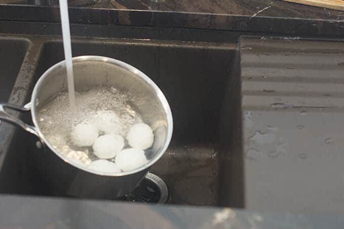 Saucepan with eggs being filled with water from tap.