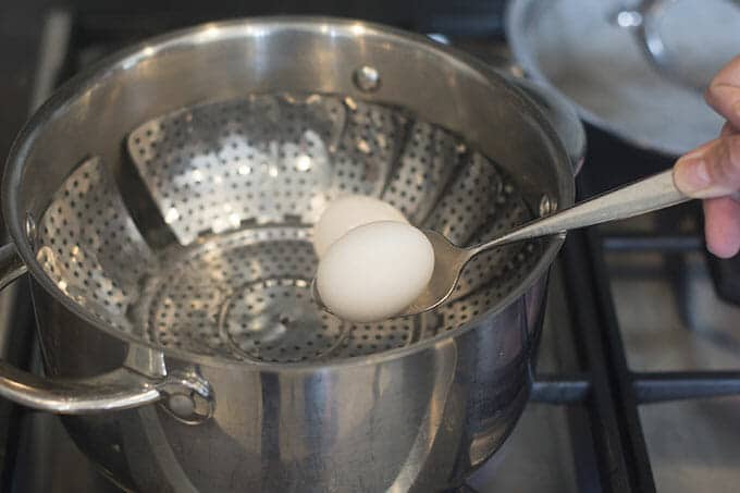 Eggs being added to steamer basket with spoon.