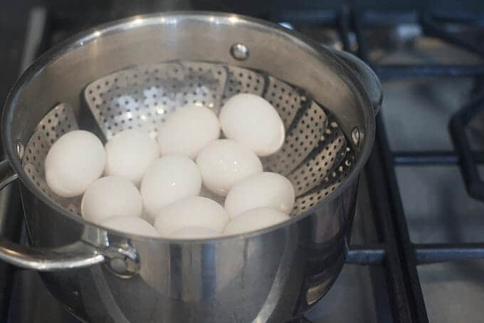 A dozen eggs in a steamer basket in a pot on the stove.