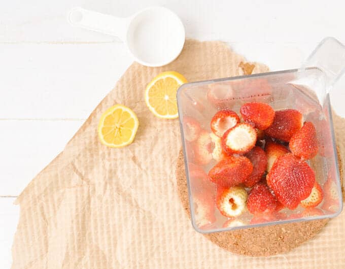 Fresh strawberries in a blender with lemons to the side.