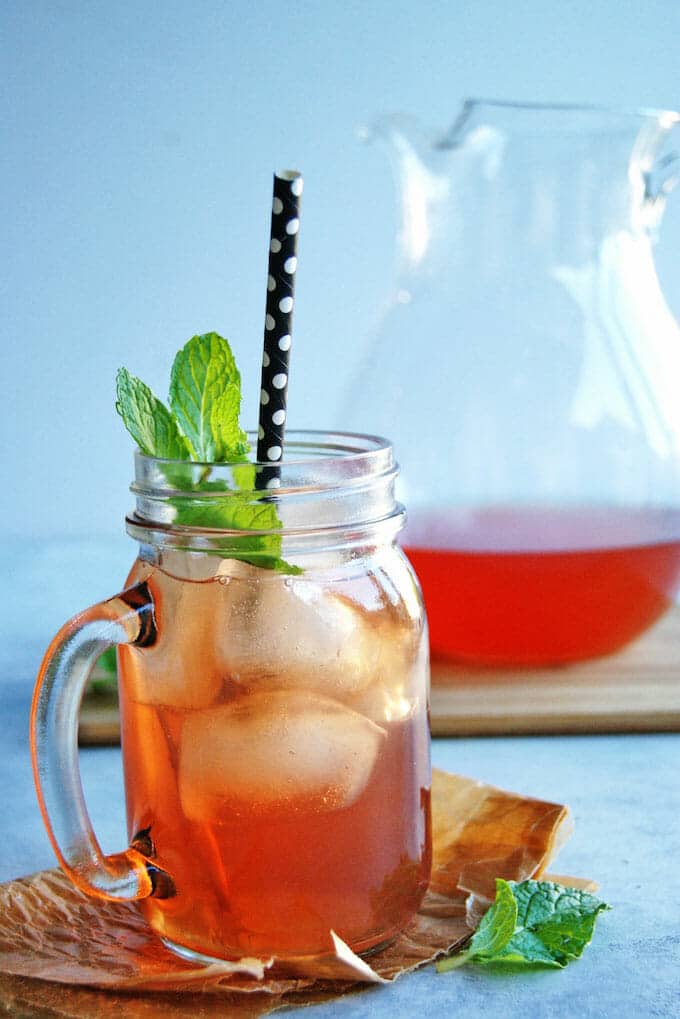 Mason jar glass with handle of iced tea with fresh mint leaves.