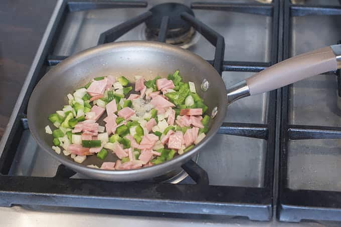 Chopped green pepper, onion, and ham in a pan on the stove.