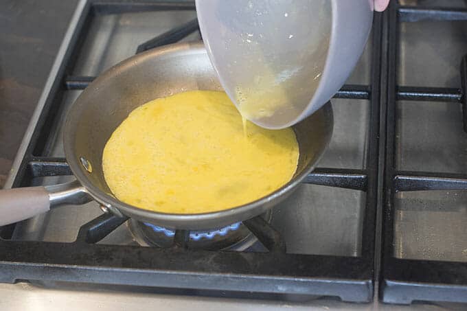 Whisked eggs being added to a pan on the stove.