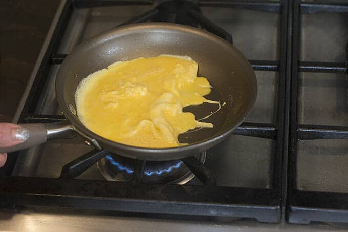 Partially cooked eggs being scraped to one side of a pan on the stove.