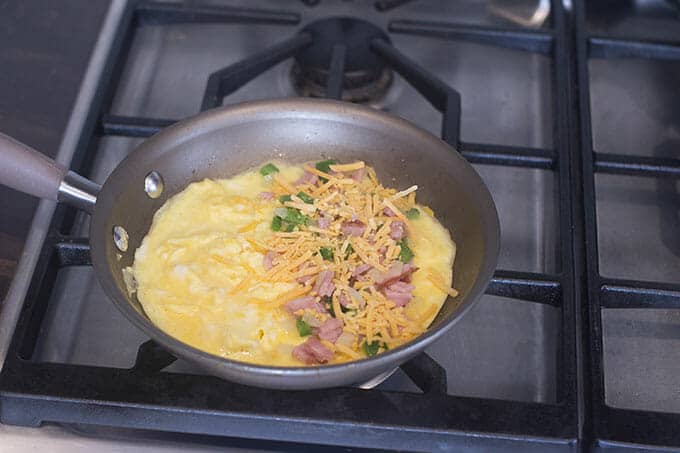Grated cheese on top of omelet filling and eggs in a pan on the stove.