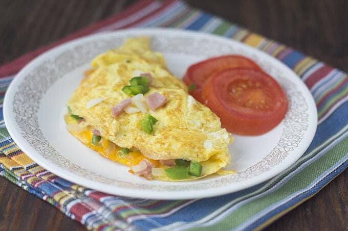 Denver omelet on a white plate with slices of tomato.