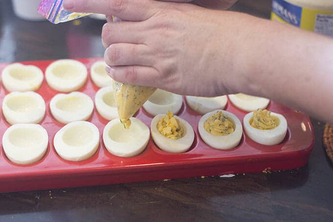 Egg yolk mixture being piped into egg white halves in a tray.