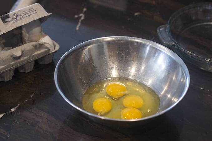 Four eggs that have been cracked into a metal bowl.