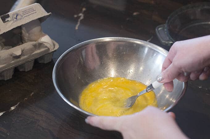 Beating eggs with a fork in a metal bowl,