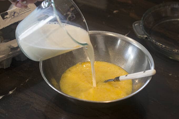 Milk being poured from a measuring cup into beaten eggs in a bowl.