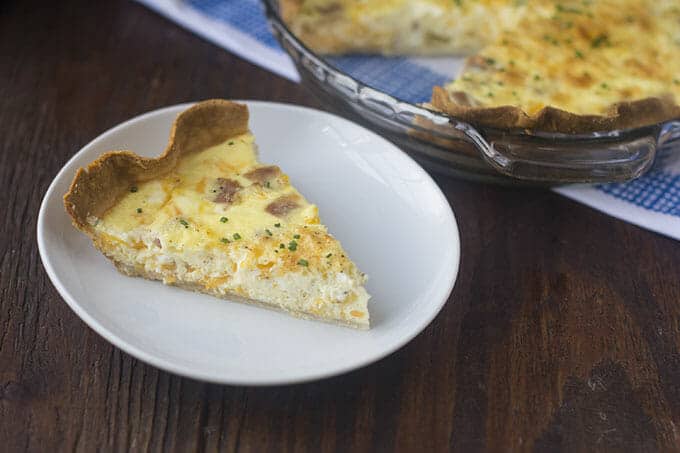 Slice of ham and cheese quiche on a white plate.