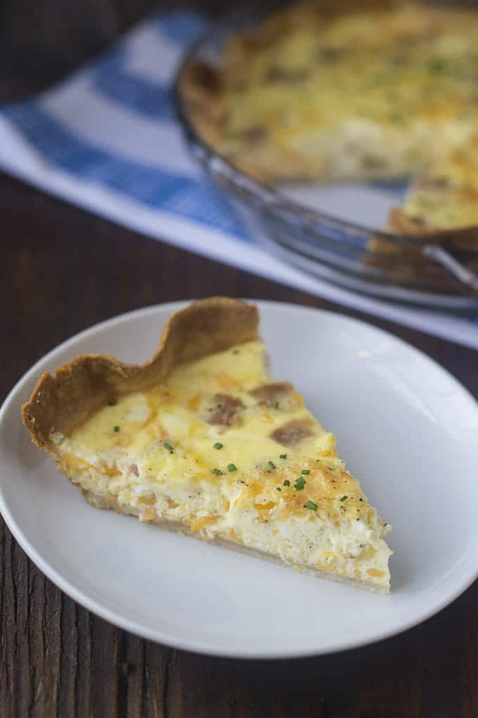 Slice of quiche with ham and cheese on a white plate.