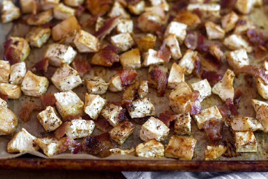 Cubed roasted vegetables and chopped bacon on a baking sheet.