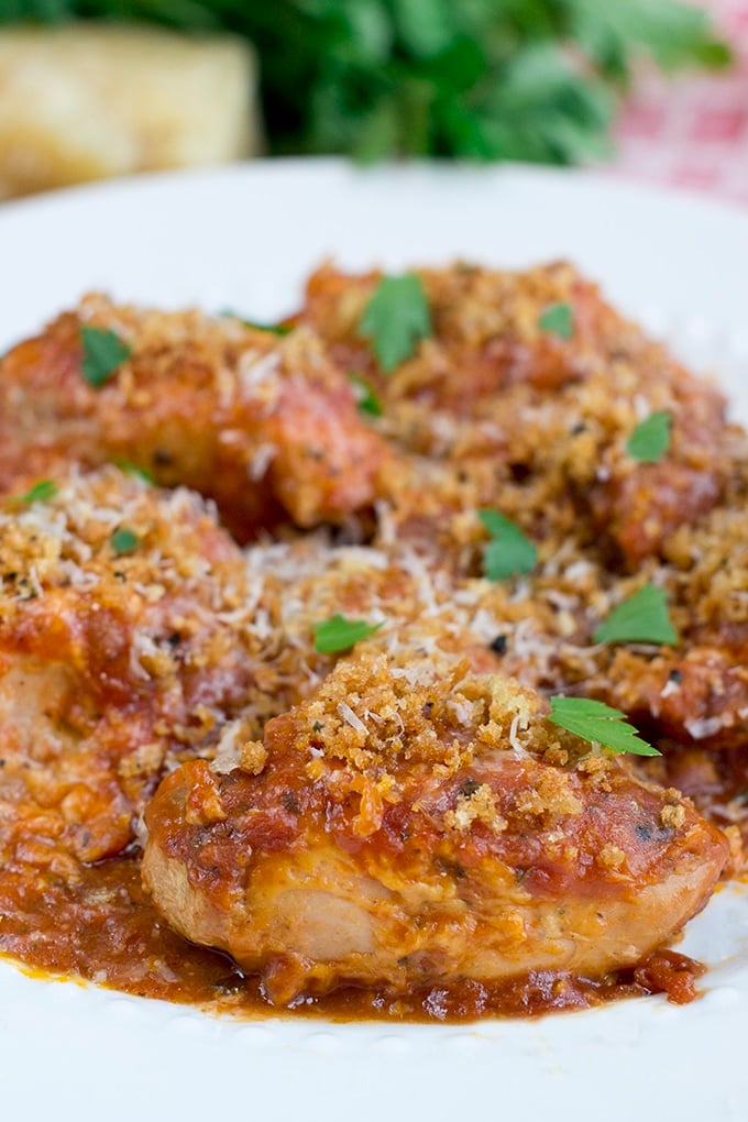 Chicken Parmesan with extra sauce and fresh parsley garnish on a white plate.