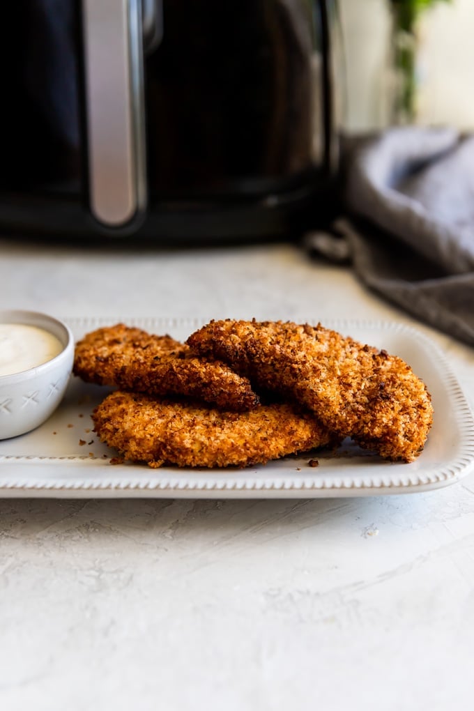 Chicken tenders on a white platter with a dipping sauce.