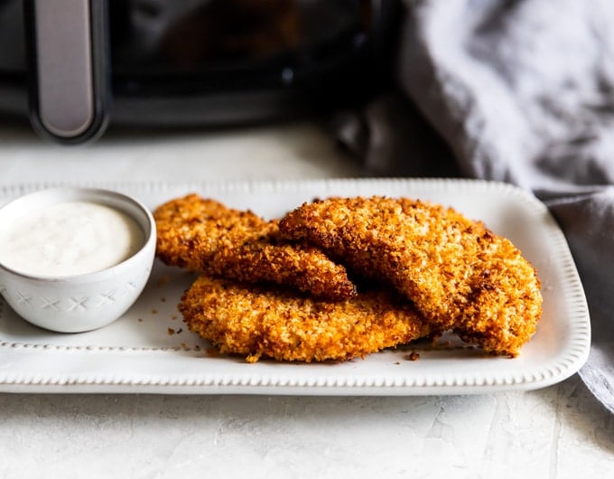 Chicken tenders on a white platter with a dipping sauce.