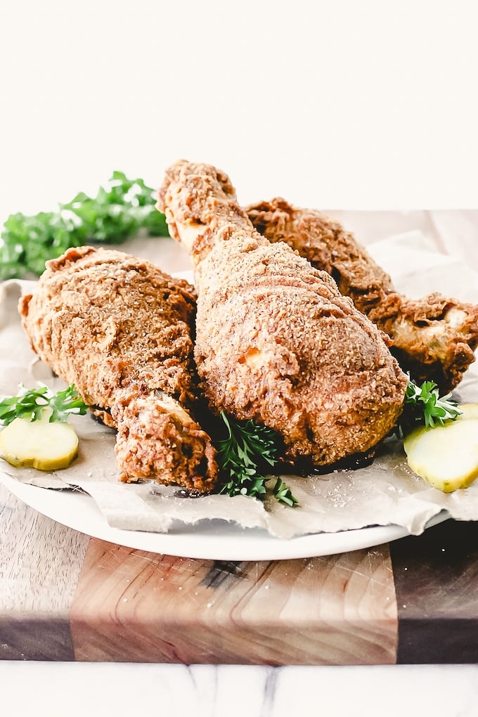 Three pieces of fried chicken sitting on butcher paper garnished with parsley sprigs and pickle slices.