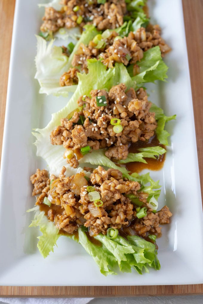 Long, rectangular white plate filled with chicken lettuce wraps that have been sprinkled with sesame seeds.