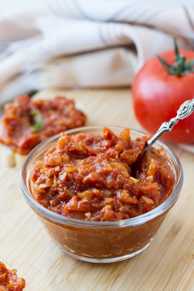 tomato chutney in a small glass bowl with a silver spoon sticking out of it.
