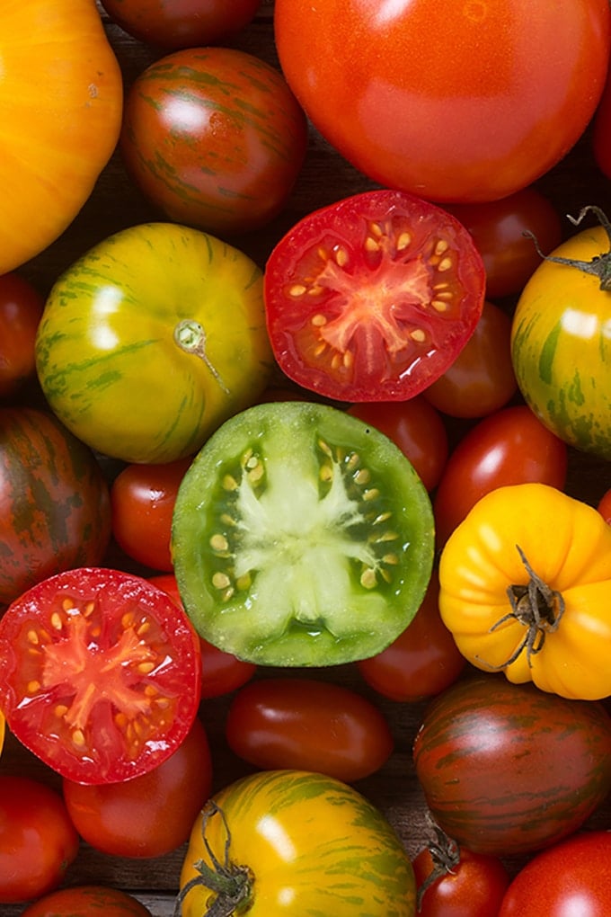 Close up of a variety of different colored and sized tomatoes; some are cut in half.